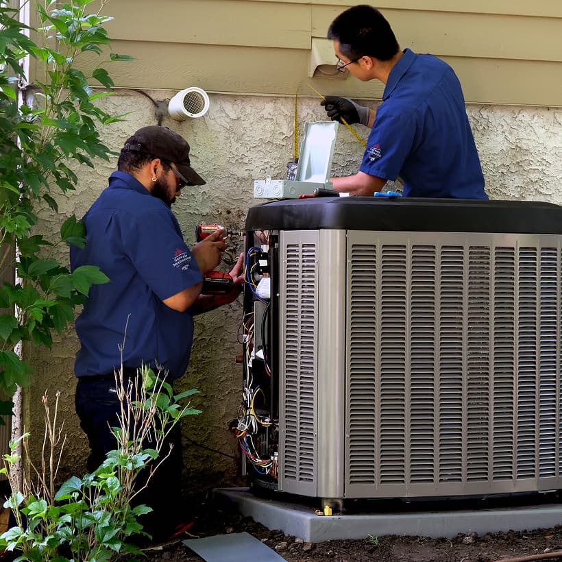 Two Gervais HVAC technicians installing a brand-new residential outdoor air conditioning condenser unit during a home AC replacement service.
