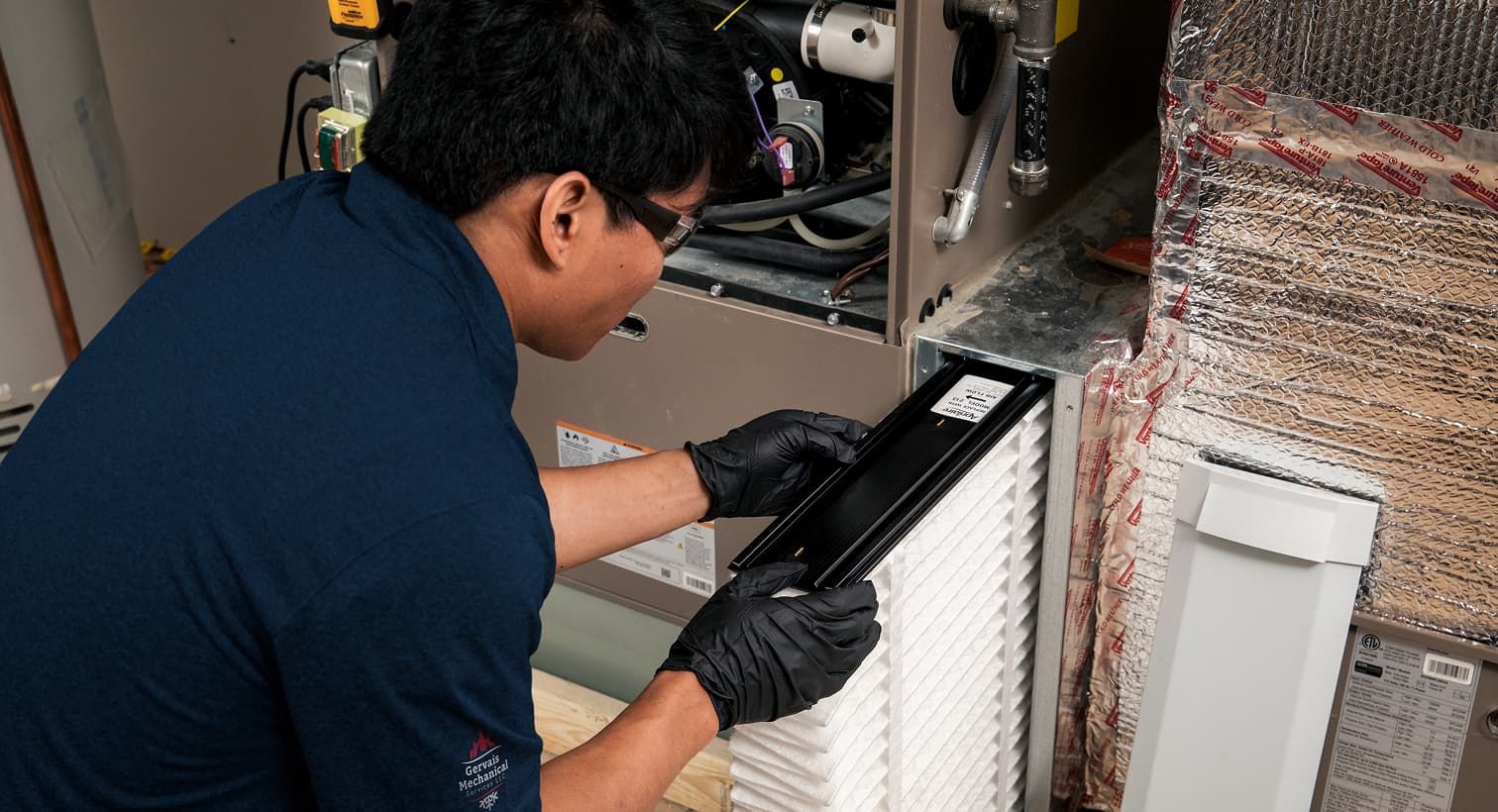 A professional Gervais HVAC technician replacing a clean pleated air filter in an indoor air handler unit during a routine AC maintenance tune-up.